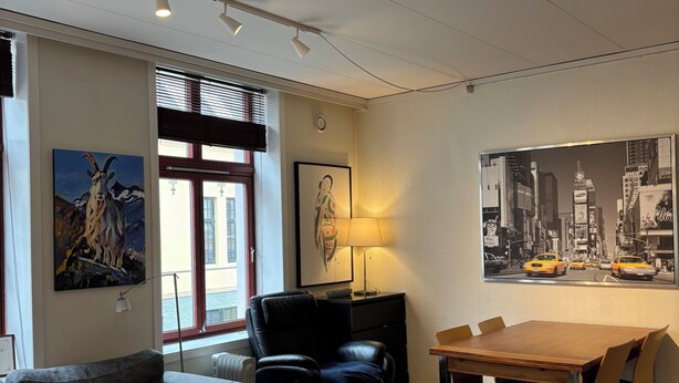 Ein modernes Wohnzimmer mit einer Couch, einem Esstisch mit Stühlen, einem schwarzen Ledersessel, einem Glastisch und einem Lampenschirm sowie einem Stadtbild.