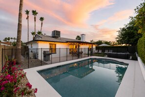 Ein modernes Haus mit Swimmingpool, überdachter Terrasse und umzäunter Garten.