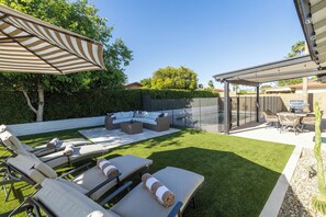 Ein Garten mit Terrasse, Gartenmöbeln und einer überdachten Sitzgelegenheit.