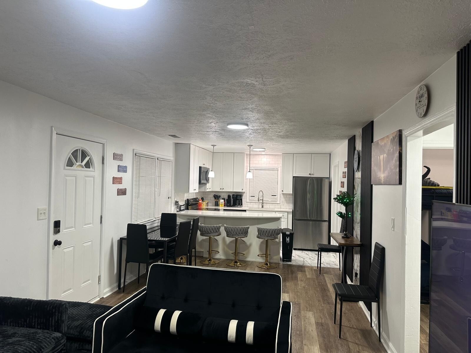 A modern kitchen with white cabinets, a stainless steel refrigerator, and a dining area with black chairs.