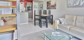 Ein modernes Wohnzimmer mit einem Glastisch, einem beigen Sofa und einem Essbereich mit Holztisch und Stühlen.