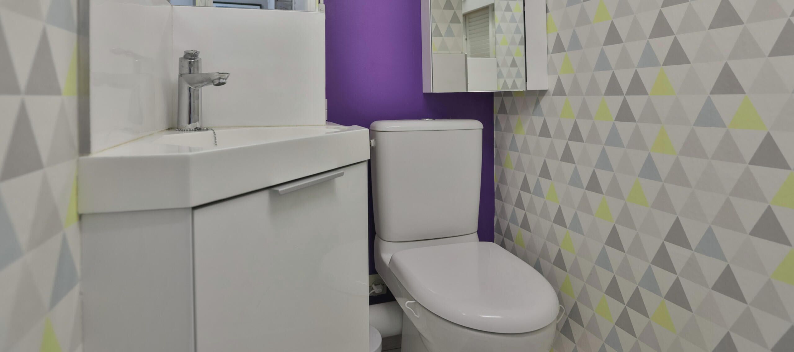 Ein Badezimmer mit einem weißen Waschbecken, einer Toilette und einer violetten Wand.