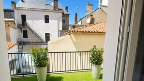 A balcony with artificial grass, two potted plants, a metal railing, and a view of neighboring buildings. - Loft Sablais - Plein centre - Parking- Plage (Les Sables-d´Olonne)