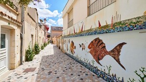 A narrow cobblestone street with buildings on either side, a tiled wall with fish murals, and a clear sky. - Loft Sablais - Plein centre - Parking- Plage (Les Sables-d´Olonne)