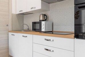Eine moderne Küche mit weißen Schränken, einem Edelstahl-Wasserkocher, einer Mikrowelle und einer Holzausziehtafel.