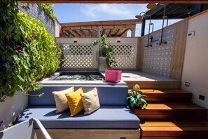 Eine Terrasse mit blauer Couch, Holzstufen, einem kleinen Wasserspiel und einer Pergola.
