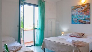 Ein Zimmer mit zwei Betten, einem grünen Sessel, einem Bild mit Booten und einer Glastür zum Außenbereich.