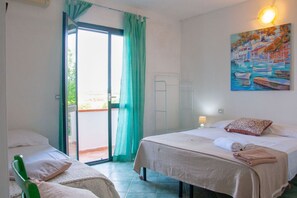 Ein Zimmer mit zwei Betten, einem grünen Sessel, einem Bild mit Booten und einer Glastür zum Außenbereich.