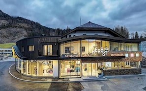 Ein modernes Gebäude mit Glasfassade, beschriftet mit 'HERB ST' und 'SKIVERLEIH', mit einem geschwungenen Design und einem Berg im Hintergrund.