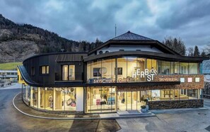 A modern building with a glass facade, labeled 'HERB ST' and 'SKIVERLEIH,' featuring a curved design and a mountain backdrop. - Autumn living experience: Apartment with 1 bedroom (Lofer)