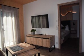 A room with a wooden cabinet, a flat-screen TV mounted on the wall, a small table, and a bed with a headboard. - Autumn living experience: Apartment with 1 bedroom (Lofer)