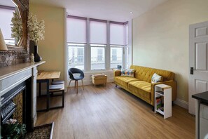 Ein Wohnzimmer mit einer Couch, einem Sessel, einem kleinen Tisch, einem Bücherregal und einem Kamin.