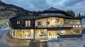 Ein modernes Gebäude mit Glasfassade, beschriftet mit 'HERB ST' und 'SKIVERLEIH', mit einem geschwungenen Design und einem Berg im Hintergrund.