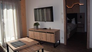 Ein Zimmer mit Holzschrank, flachbildfernseher an der Wand, einem kleinen Tisch und einem Bett mit Kopfteil.