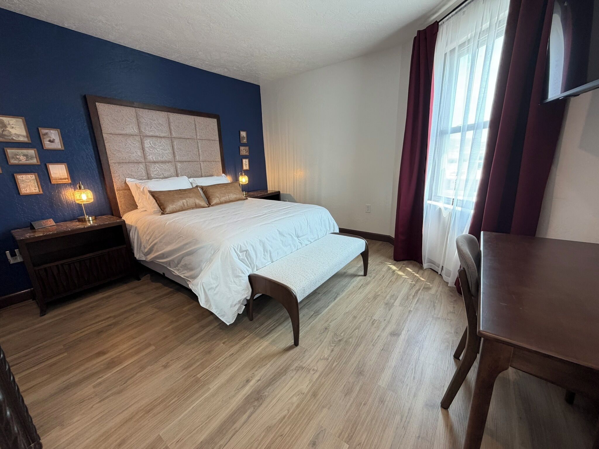A hotel room with a bed, bedside table, lamp, and a window with curtains.