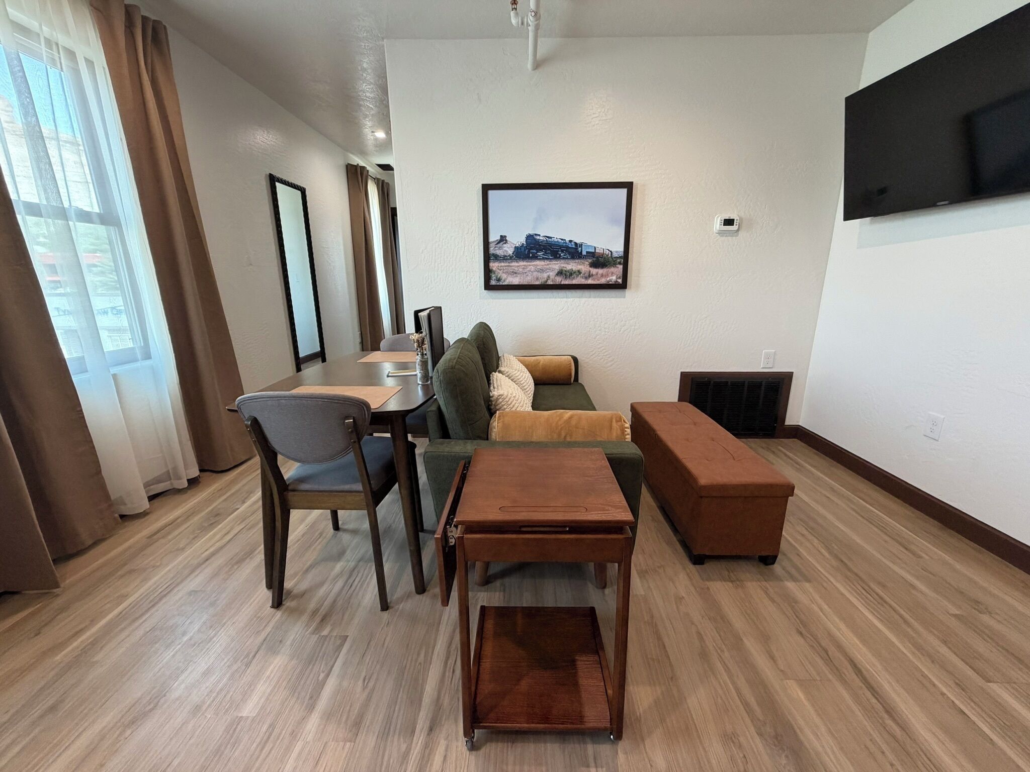 A modern living room with a dining area, a sofa, a coffee table, and a flat-screen TV mounted on the wall.