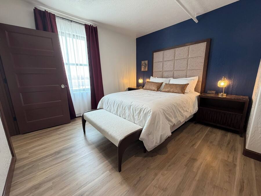 A bedroom with a bed, bench, bedside tables, and a door.