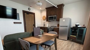 A compact kitchen with a dining area, a microwave, a refrigerator, and a TV mounted on the wall.