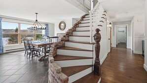 Une pièce spacieuse comprenant un coin repas, un escalier avec des rampes blanches et une vue sur l’extérieur.