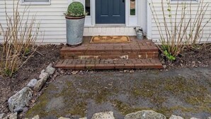 Une maison à deux étages avec une porte d’entrée sombre, un petit porche et un marchepied en briques menant à la porte.