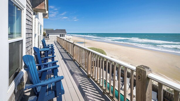 A wooden deck with blue chairs, a beach view, and a building with a balcony. - Beachfront Oasis w Dune Walkover, Pool n Spa & More! (Corolla)