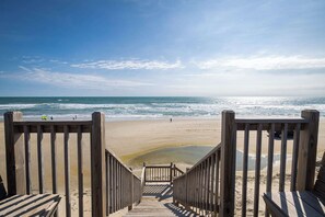 Eine Holztreppe führt zu einem Strand unter blauem Himmel.
