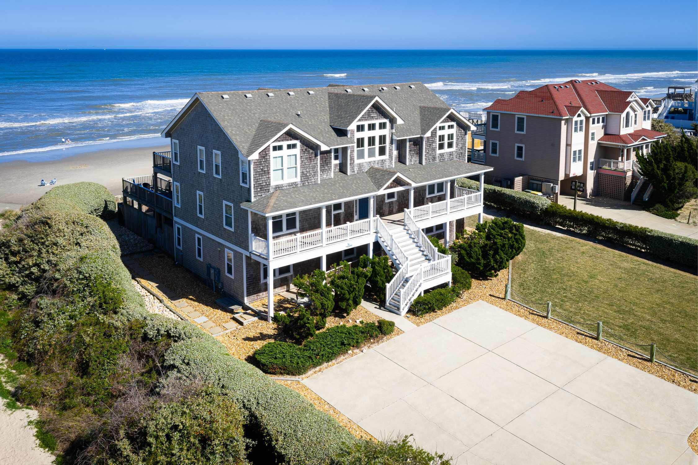 A beachfront property with multiple houses, a large driveway, and a view of the ocean.