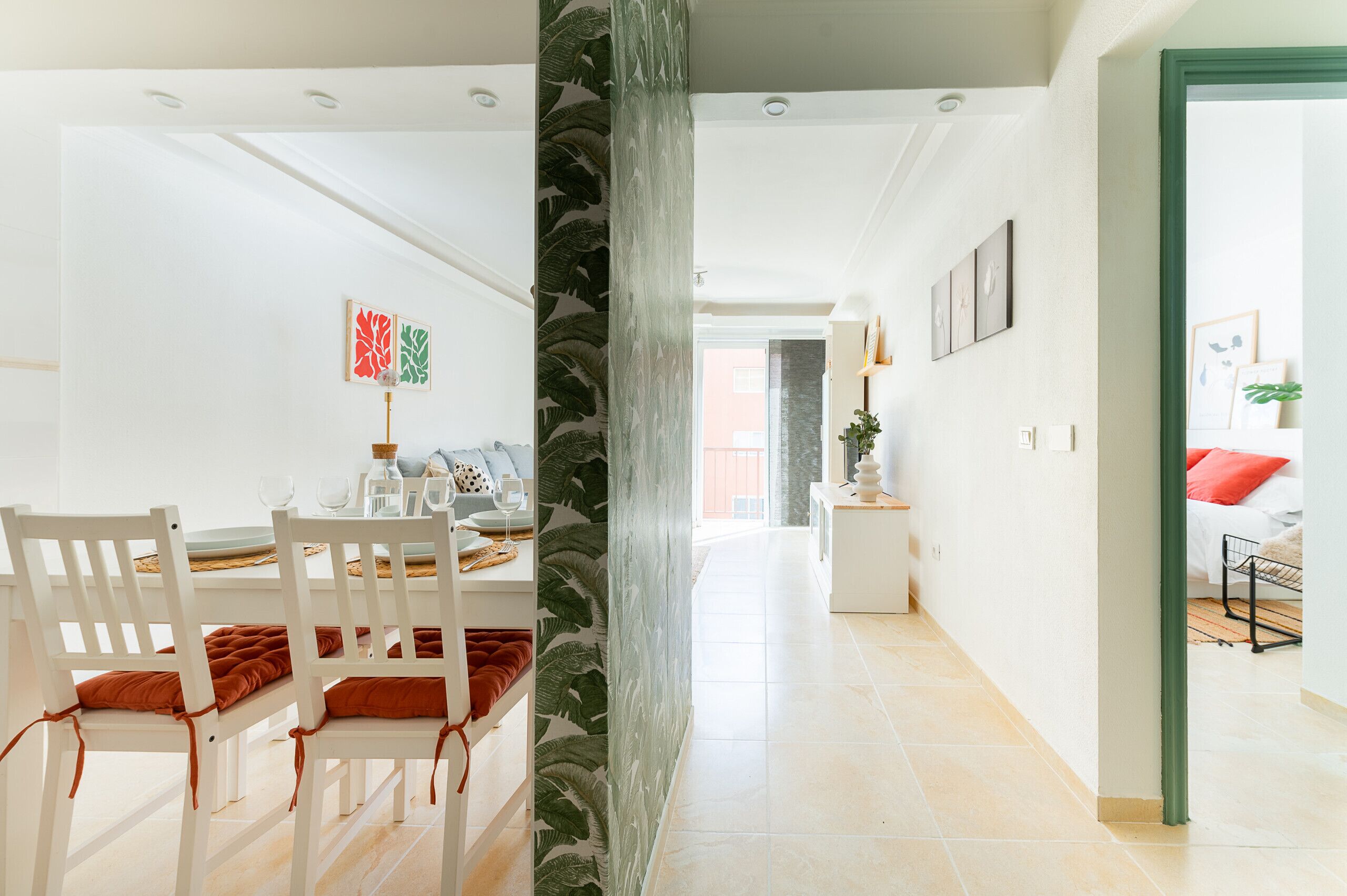 A modern dining area with white furniture and a view into a living space.