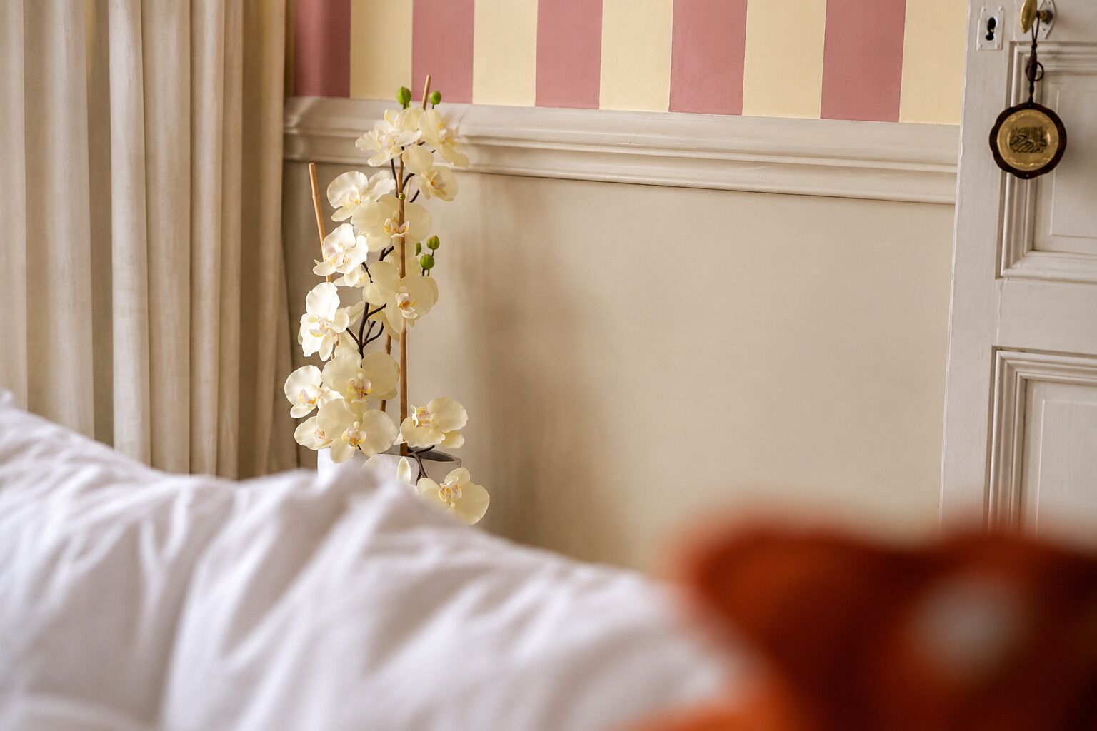 Een slaapkamer met een bed, een witte orchidee en een gestreepte wand.