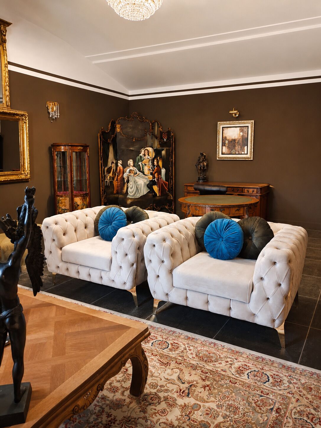 A room with a large painting, a chandelier, and a sofa with decorative pillows.