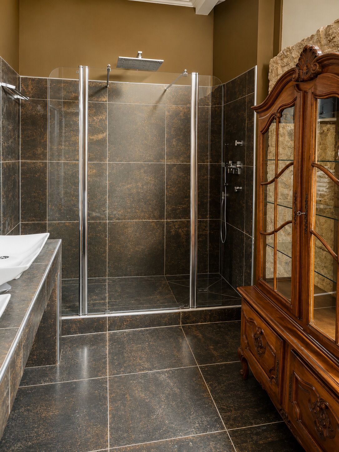 Un baño con ducha envuelta en vidrio, un mueble de madera y suelo de baldosas oscuras.