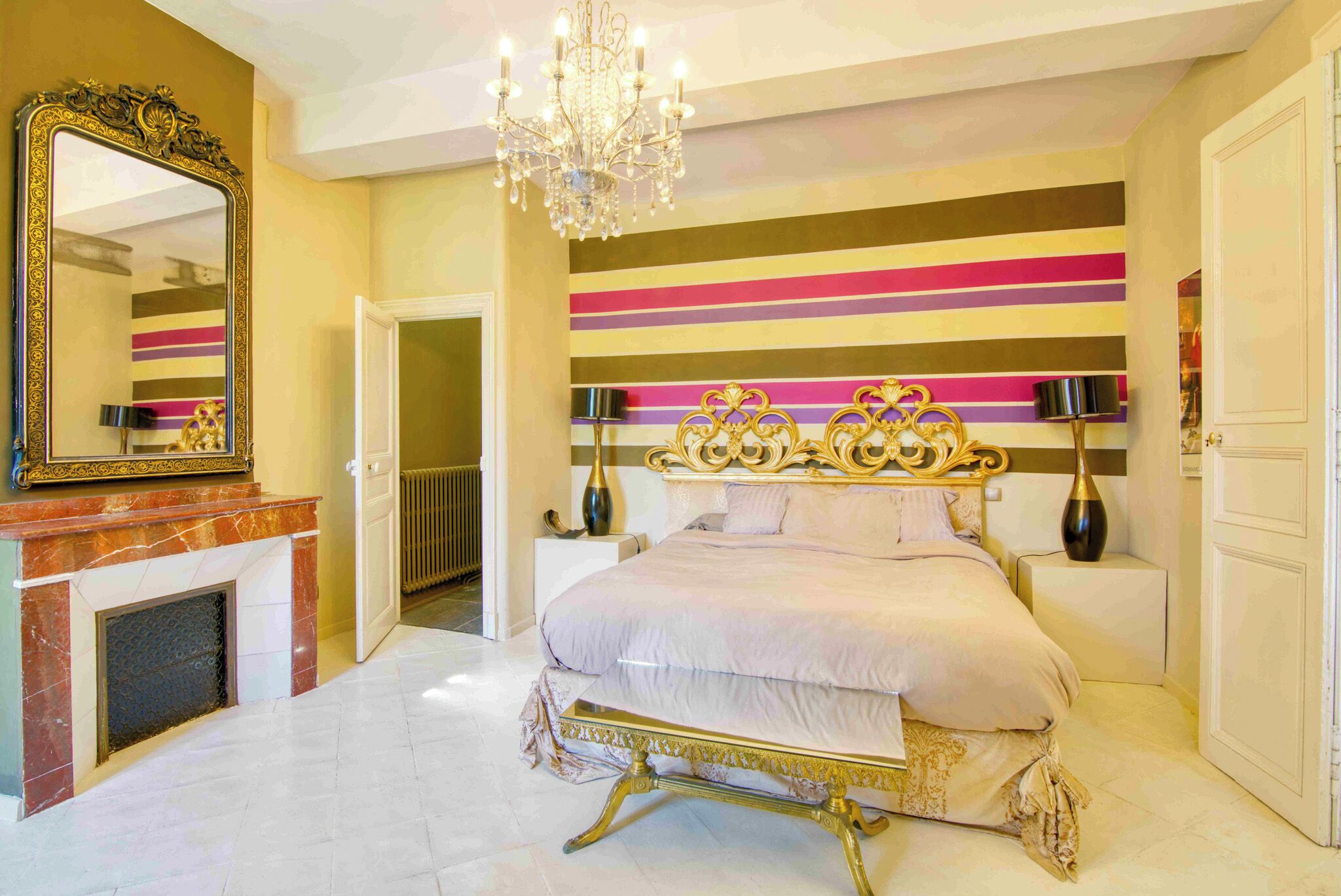 A bedroom with a large bed, a chandelier, a fireplace, and a striped wall.