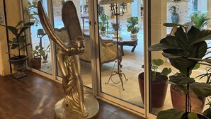 Ein Zimmer mit einer großen Glasdoor, die auf eine Außenpatio führt, einer Bronze-Statue und mehreren Kübelpflanzen.