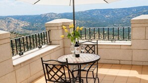 Ein runder Tisch mit Stühlen, einer Weinflasche und einem Blumenstrauß auf einem Balkon mit Bergblick.