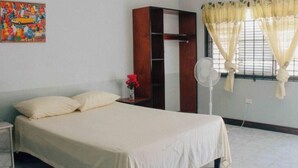 A bedroom with a bed, a wardrobe, a fan, and a window with curtains. - Grassroots Negril (Negril)