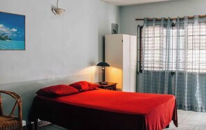Una habitación con cama, lámpara, armario y ventana con cortinas.