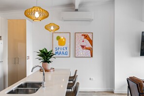 A modern kitchen with a central island, pendant lights, and two framed pictures on the wall. - Lakeside 2-Bed Retreat with Sunny Balcony (Buff Point)