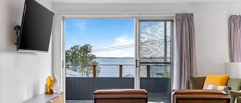Una habitación con un gran ventanal corredero que da a un balcón, un televisor de pantalla plana montado en la pared y una zona de estar con una mesa y sillas.