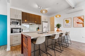 A modern kitchen with a central island, bar stools, and pendant lighting. - Lakeside 2-Bed Retreat with Sunny Balcony (Buff Point)