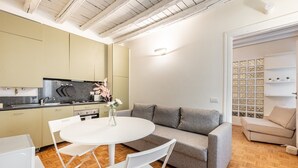 Moderni keittiö, jossa on ruokapöytä ja -tuolit, harmaa sohva ja valkoinen seinä, jossa on koristeellinen paneeli.