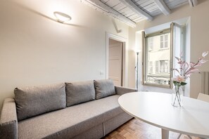 Ein modernes Wohnzimmer mit einem grauen Sofa, einem runden weißen Tisch und einer Vase mit Blumen.
