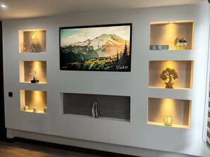 Eine Wand mit einem Flachbildfernseher, mehreren beleuchteten Regalen und einem Kamin.