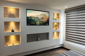 Ein modernes Wohnzimmer mit flachbildfernseher an der Wand, umgeben von beleuchteten Regalen mit verschiedenen Gegenständen.