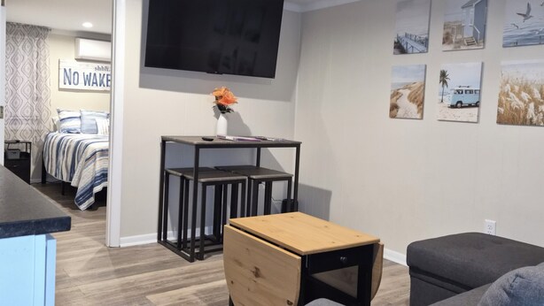 A modern living room with a flat-screen TV, a wooden coffee table, a grey sofa, and a small desk with a chair.