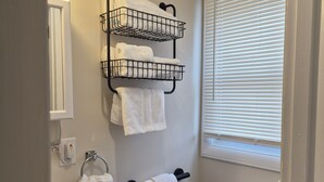 A bathroom with a toilet, sink, towel rack, and a window with blinds.
