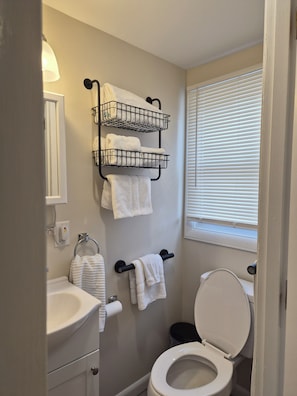 Ein Badezimmer mit Toilette, Waschbecken, Handtuchhalter und einem Fenster mit Jalousien.