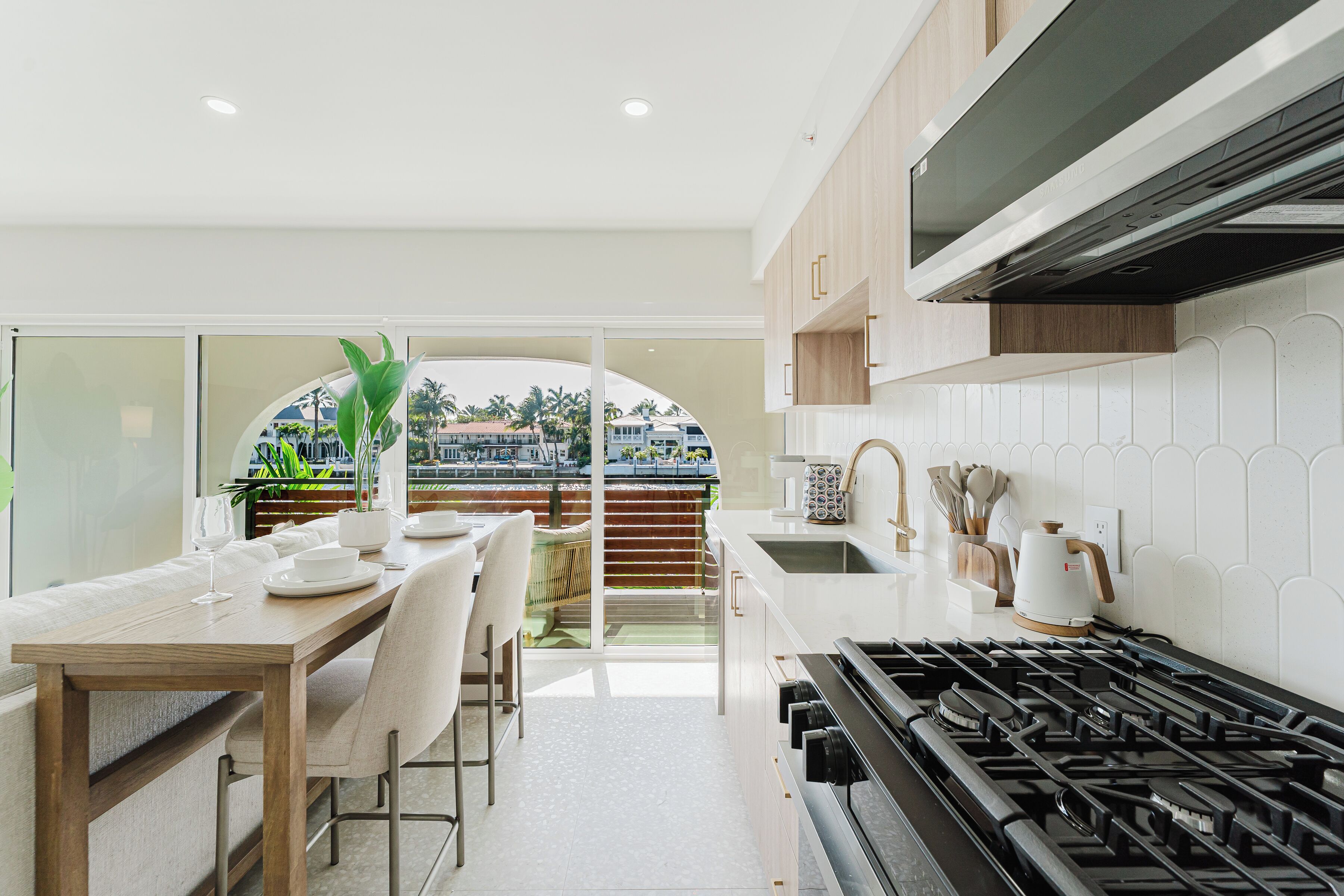 A modern kitchen with a dining area, a view through a glass door, and a stove.