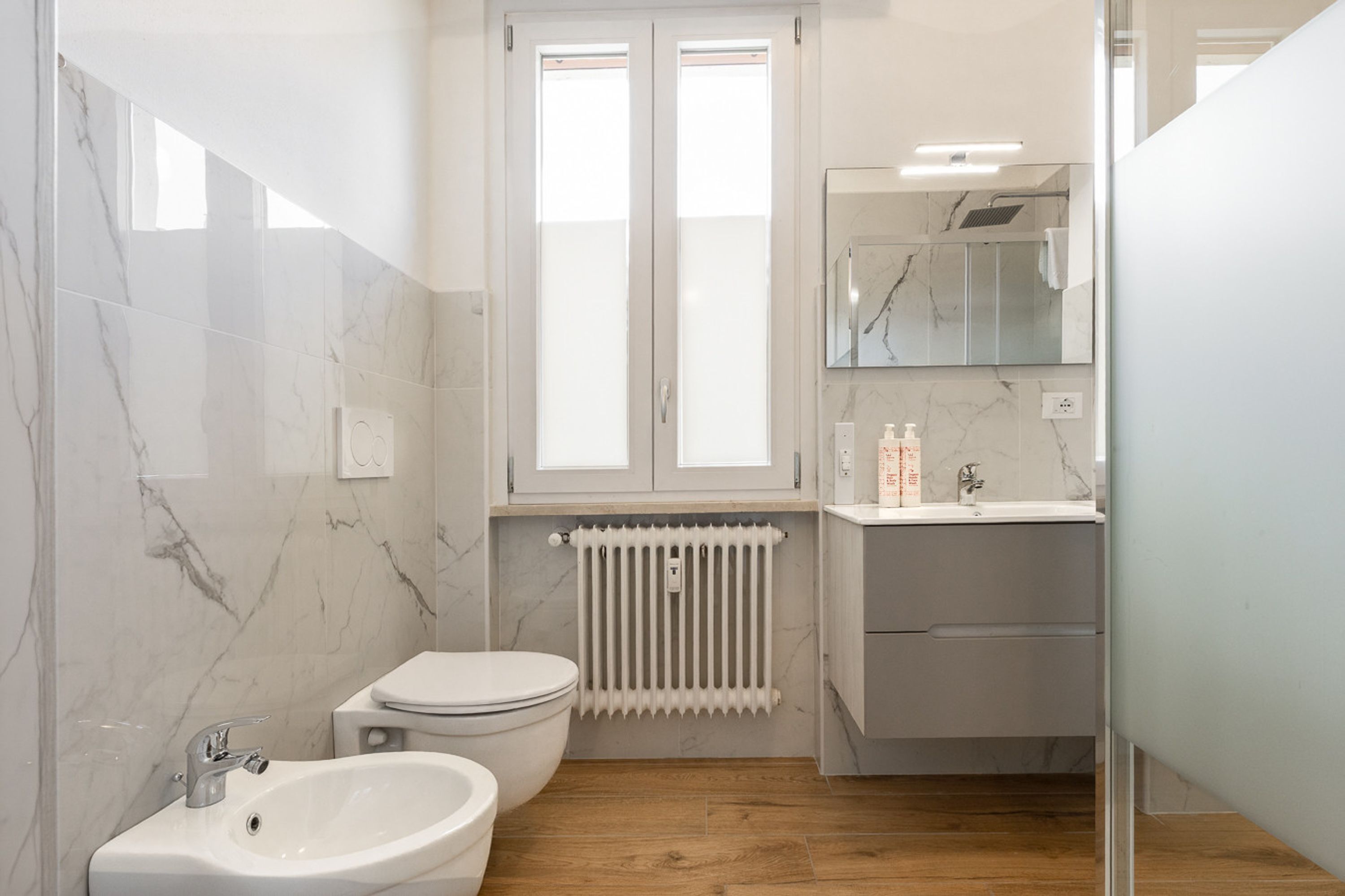 Une salle de bain équipée de toilettes, d’un bidet, d’un lavabo, d’un miroir et d’un radiateur.