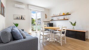 A modern living room with a grey sofa, white chairs, a wooden dining table, and a kitchen area with shelves and a radiator. - Sogno del Garda by Wonderful Italy (Desenzano del Garda)