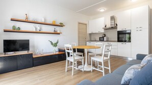 A modern living room with a flat-screen TV, wooden dining table, white chairs, and a grey sofa. - Sogno del Garda by Wonderful Italy (Desenzano del Garda)